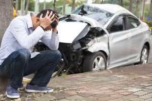 Man with his head in his hands sitting outside of a wrecked car