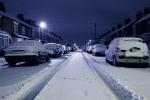 A snowy street with cars parked on either side.