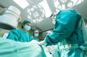 Three people in scrubs and masks in an operating room performing surgery