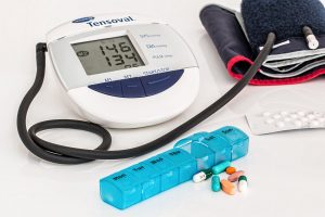 A blood pressure monitor, pill case, and medications on a table