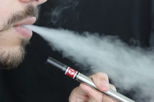 A man holding an e-cigarette and exhaling